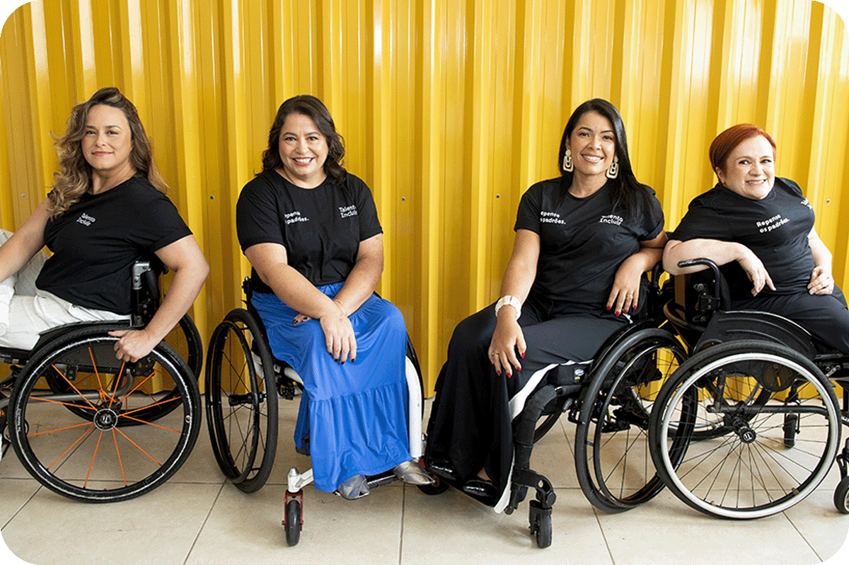Foto das quatro consultoras da Talento Incluir. Todas estão sentadas em suas cadeiras de rodas, posando sorridentes lado a lado. Atrás delas uma parede de metal amarela. Foto das quatro consultoras da Talento Incluir. Todas estão sentadas em suas cadeiras de rodas, posando sorridentes lado a lado. Atrás delas uma parede de metal amarela.